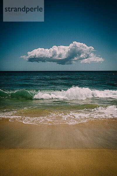 Eine einsame Wolke schwebt über den Wellen und dem Sand des blauen Pazifiks