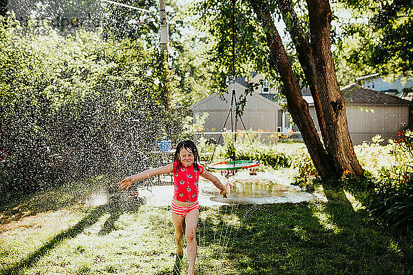 Junges Mädchen läuft im Sommer durch Sprinkleranlage im Hinterhof