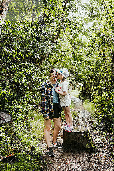 Junges Mädchen küsst ihrer Mutter während einer Wanderung im Wald die Wange