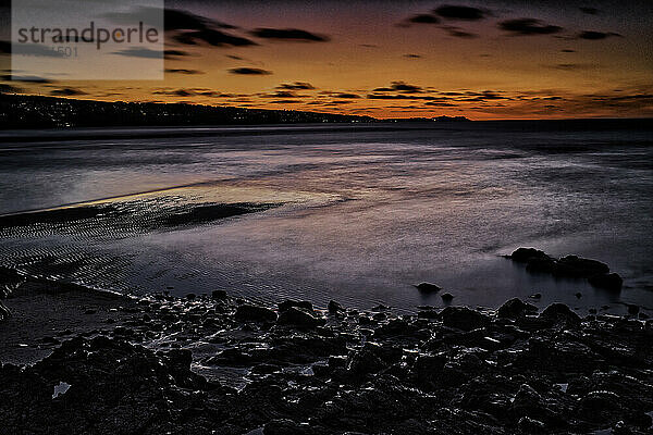 Sonnenuntergang über Strand und Meer mit Felsen im Vordergrund