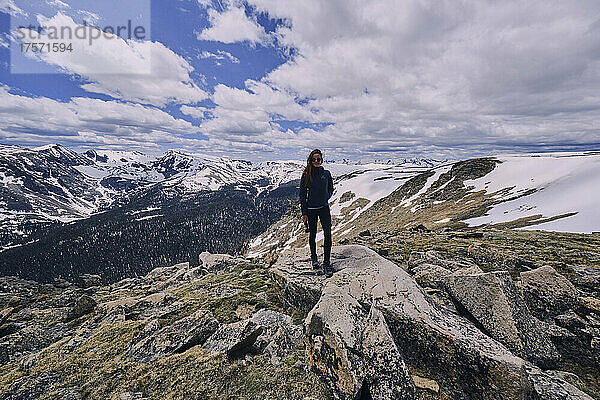 Junge Frau steht auf freiliegendem Felsen in einem Schneefeld in den Rocky Mountains