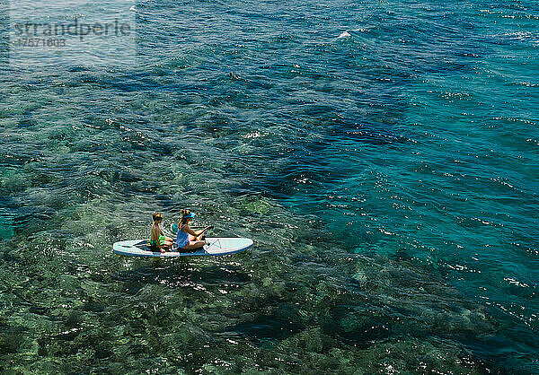 Mutter und Sohn stehen beim Stand-Up-Paddle-Boarding über den Korallenriffen des Ozeans