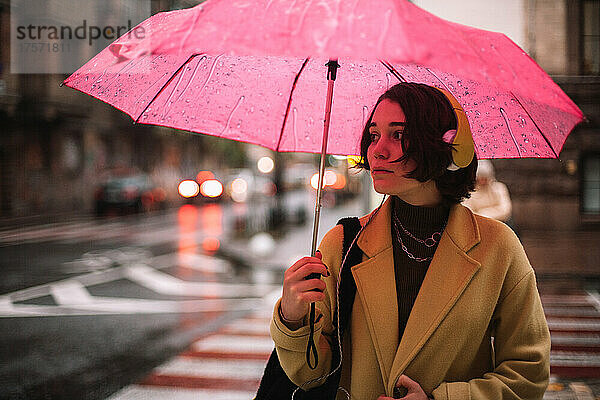 Junge Frau mit Regenschirm steht im Herbst auf der Straße in der Stadt