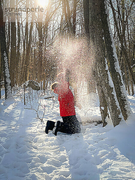 Kleiner Junge im roten Wintermantel spielt im Schnee im Wald.