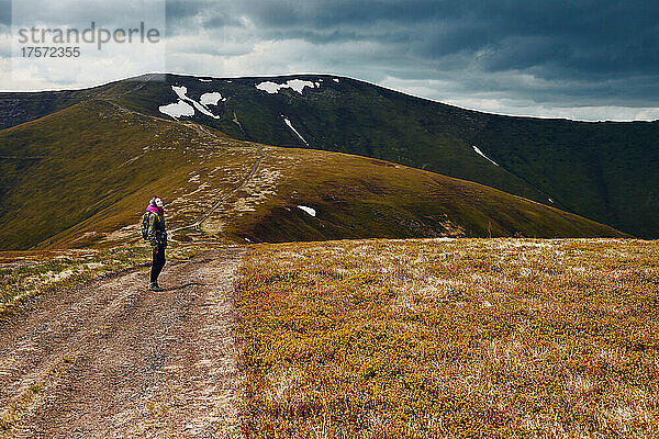 Eine Frau geht einen Bergpfad entlang einer Bergkette entlang.