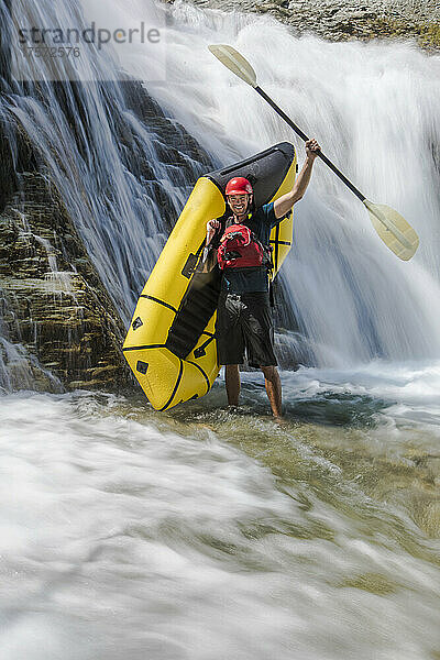 Paddler steht neben Wasserfall und hebt Paddel in die Luft.