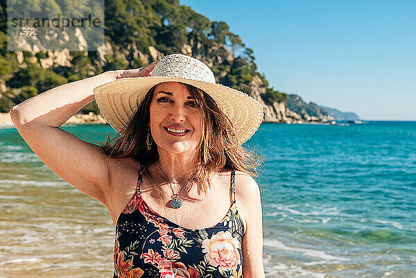 50-jährige Frau geht mit Hut am Strand spazieren