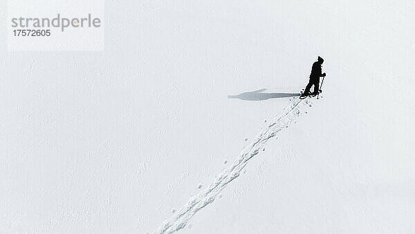 Luftaufnahme eines Mannes  der mit Schneeschuhen über eine leere verschneite Landschaft wandert.