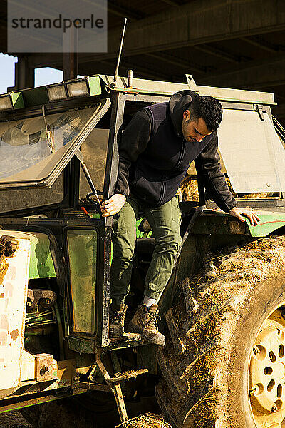 Junger Bauernjunge steigt während der Arbeit auf dem Bauernhof vom Traktor ab