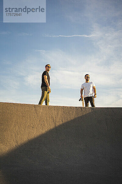 Freunde stehen oben auf einer Skateboardrampe und blicken auf den Horizont