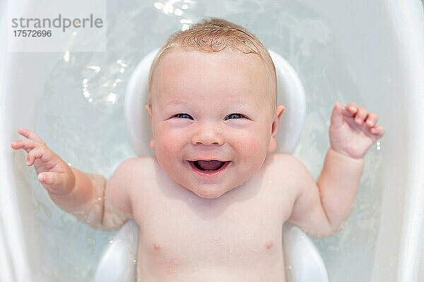 Fröhliches Baby im Alter von 6 Monaten badet in einer Babybadewanne