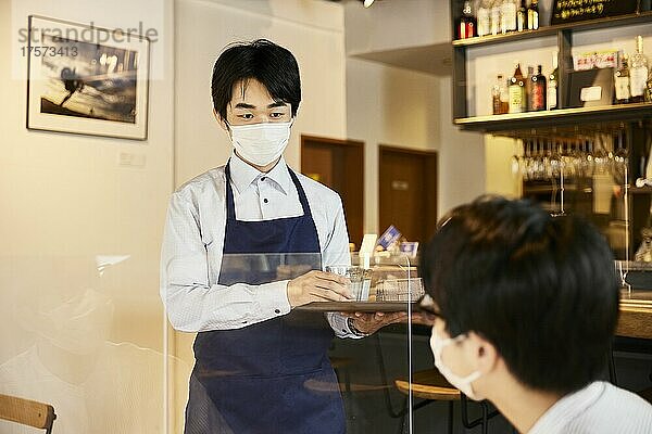 Japanische männliche Kellnerin serviert kalte Getränke