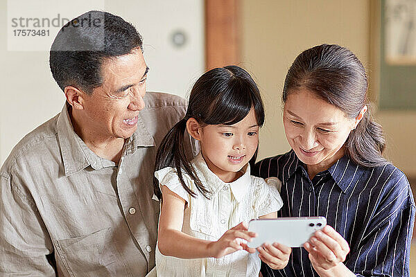 Japanische Großeltern und Enkelkinder bedienen ein Smartphone