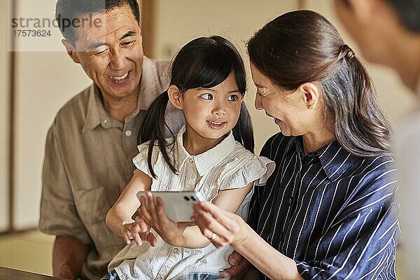 Japanische Großeltern und Enkelkinder bedienen ein Smartphone