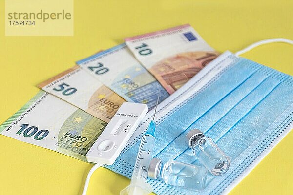 Geld (Euro-Banknoten) mit medizinischen Masken  Antigentest  Impfstoffflaschen und Spritze. Finanzkrise aufgrund von Coronavirus-Verlusten  selektiver Fokus