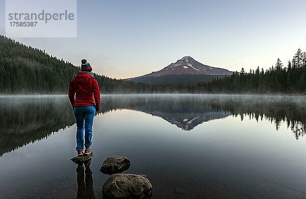 Junge Frau steht auf einem Stein  Spiegelung des Vulkans Mt. Hood im See Trillium Lake  bei Sonnenaufgang  Oregon  USA  Nordamerika
