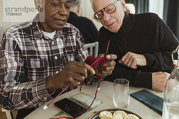 Älterer Mann strickt mit einem männlichen Freund im Altersheim