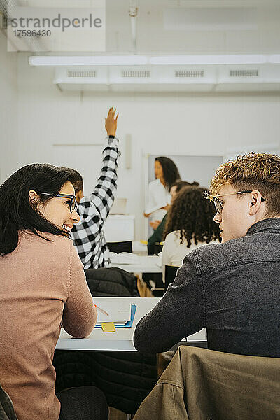 Rückansicht eines männlichen und eines weiblichen Schülers  die sich unterhalten  während sie zusammen im Klassenzimmer sitzen