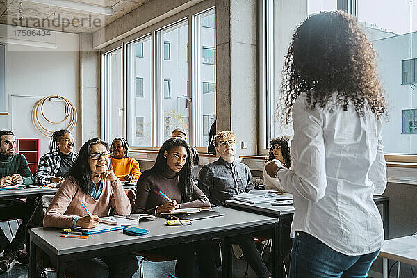Rassisch gemischte Studenten hören einem Professor zu  der in einem Klassenzimmer einer Volkshochschule unterrichtet