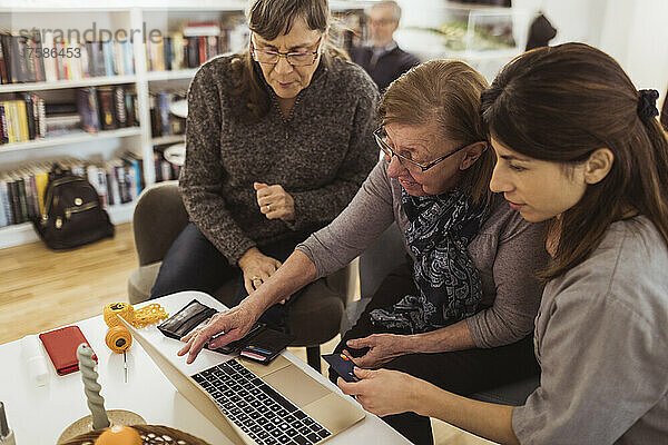 Ältere Frau lernt Online-Shopping am Laptop von einer Pflegekraft im Pflegeheim