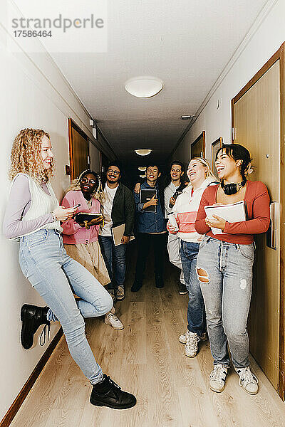 Multirassische Studenten  die eine Freundin ansehen und über den Gang im Studentenwohnheim lachen