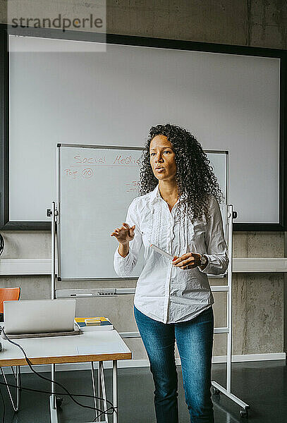 Selbstbewusster Lehrer mit lockigem schwarzem Haar  der vor einer Tafel im Klassenzimmer einer Hochschule erklärt