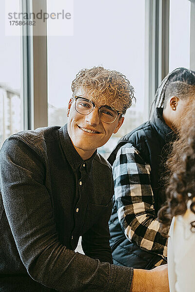 Porträt eines lächelnden blonden Mannes mit Brille  der in der Cafeteria einer Universität sitzt