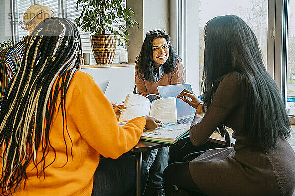 Lächelnde reife Studentin  die mit Freunden in der College-Cafeteria diskutiert