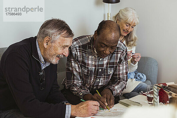 Lächelnde ältere Männer  die von einer Freundin im Pflegeheim auf Papier gezeichnet werden