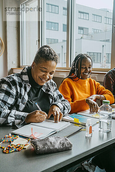 Lächelnde Studentinnen lernen gemeinsam in einem Klassenzimmer einer Volkshochschule