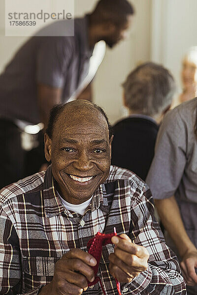 Porträt eines lächelnden älteren Mannes  der im Altersheim strickt