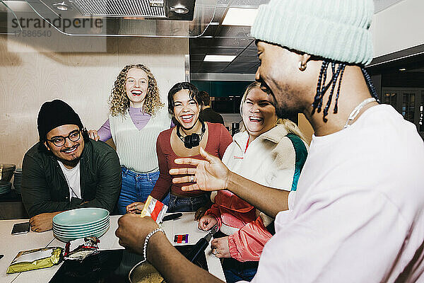 Glücklicher multirassischer junger Mann und Frauen  die einen männlichen Freund bei der Zubereitung von Essen im Studentenwohnheim beobachten
