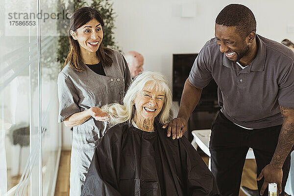 Fröhliche männliche und weibliche Pflegekräfte im Gespräch mit einer älteren Frau im Pflegeheim