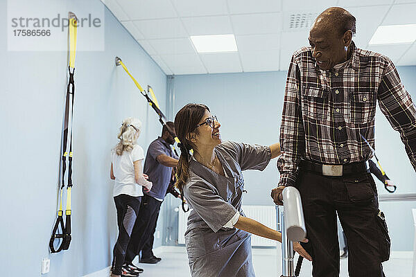 Eine lächelnde Pflegerin hilft einem älteren Mann im Pflegeheim beim Gehen