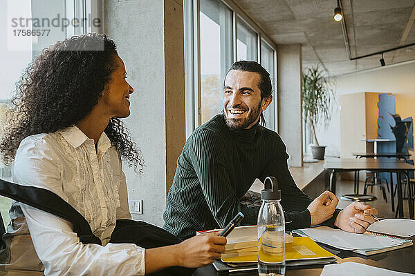Lächelnder junger Mann  der seine Freundin beim gemeinsamen Lernen in der College-Cafeteria ansieht
