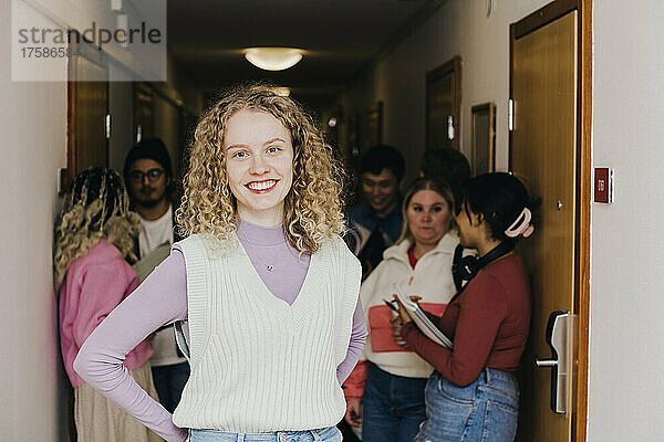 Porträt einer lächelnden jungen Frau mit multirassischen Freunden im Hintergrund auf dem Flur eines Studentenwohnheims