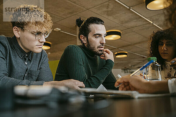 Junge gemischtrassige Studenten sitzen am Tisch und lernen zusammen in der Cafeteria