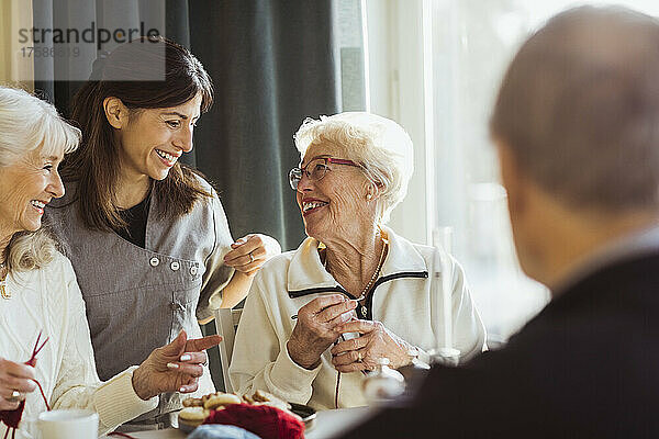 Lächelnde Krankenschwester im Gespräch mit strickenden Seniorinnen im Pflegeheim