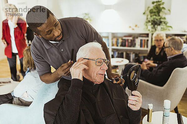 Männliche Pflegekraft im Gespräch mit einem älteren Mann beim Haareschneiden im Altersheim