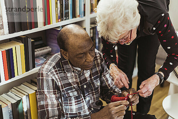 Älterer Mann strickt  während seine Freundin ihm im Altersheim hilft