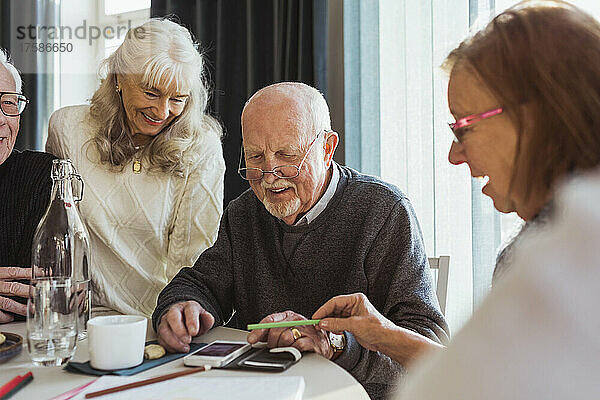 Lächelnde ältere Freunde benutzen ihr Smartphone am Tisch im Pflegeheim