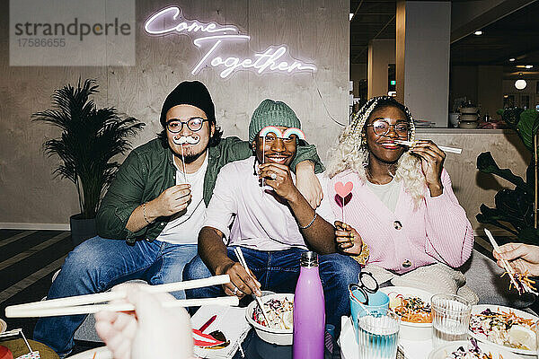 Porträt eines glücklichen multirassischen männlichen und weiblichen Freundes mit Requisiten beim Essen im Studentenwohnheim