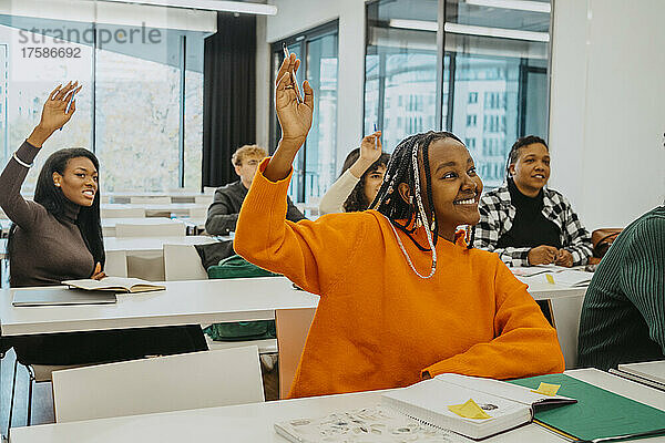 Weibliche Schüler heben die Hände  während sie im Klassenzimmer sitzen