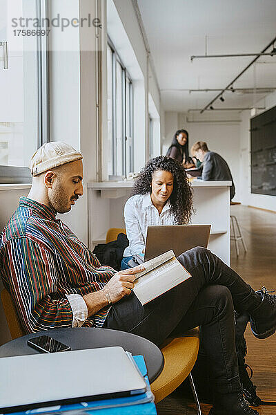 Ein Mann liest ein Buch  während eine Frau einen Laptop in der Universität benutzt