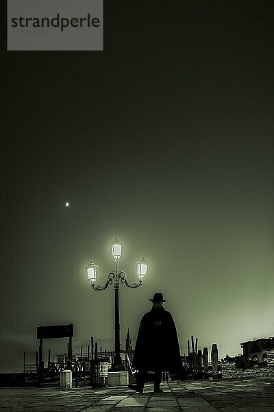 Düstere Stimmung  Mann mit Hut als Schattenriss bei blauer Stunde vor beleuchteter Straßenlaterne  Venedig  Venetien  Italien  Europa