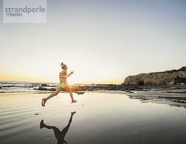 Vereinigte Staaten  Kalifornien  Laguna Beach  Rückansicht einer Sportlerin  die bei Sonnenuntergang am Strand läuft