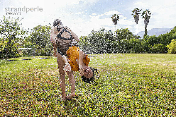 Südafrika  Westkap  Stanford  Mädchen (16-17) und Junge (8-9) spielen mit Wasser auf dem Rasen