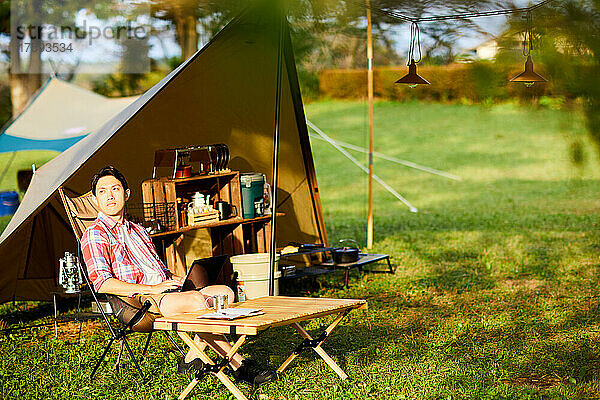 Japanischer Mann  der auf dem Campingplatz Telearbeit leistet