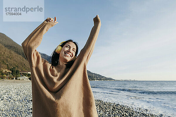 Glückliche junge Frau  die über Kopfhörer Musik hört und am Strand tanzt
