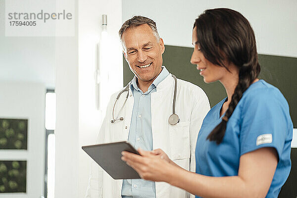 Krankenschwester diskutiert mit lächelndem Arzt über Tablet-PC im Krankenhaus